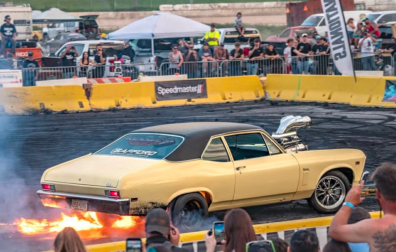 A supercharged Chevy Nova on a flaming burnout in front of the crowd at the strip