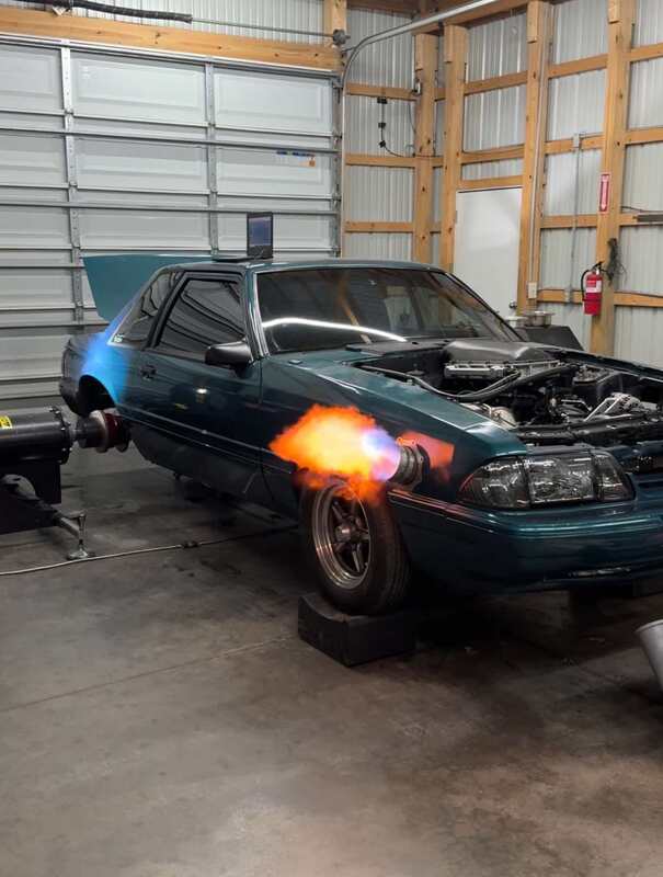 A teal Fox body notchback with the hood up and a laptop on the roof, flame out the exhaust dump