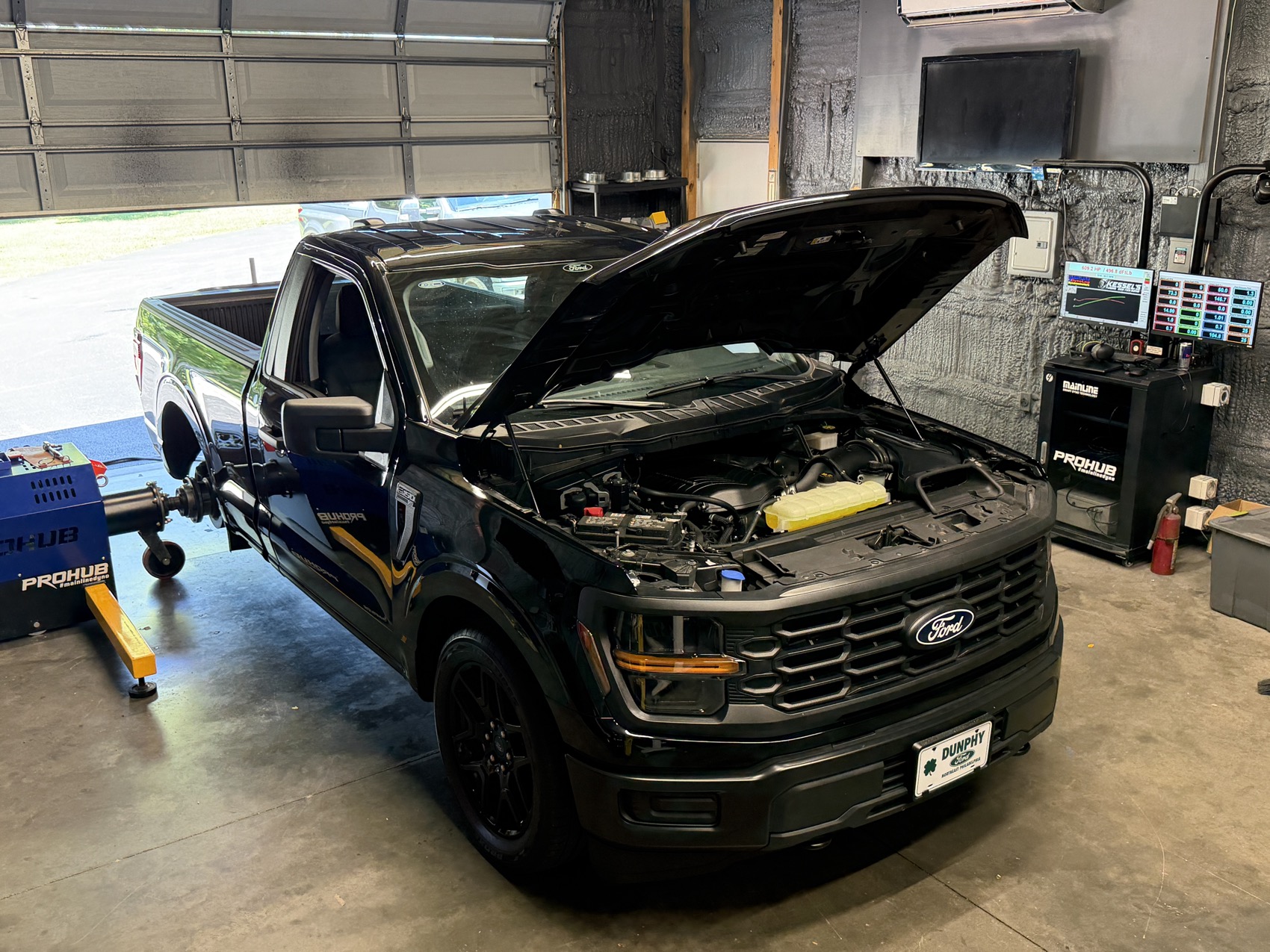 A Ford F-150 with the hood up, strapped to the dyno