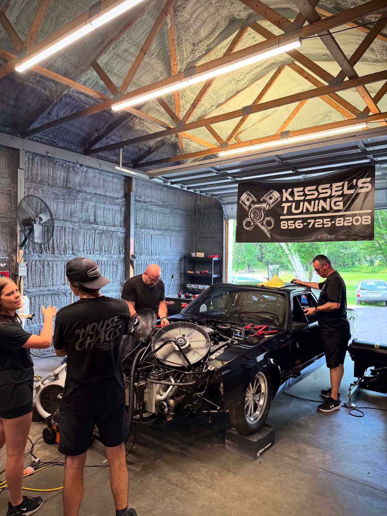 A car with the front end open on the dyno under the shop banner